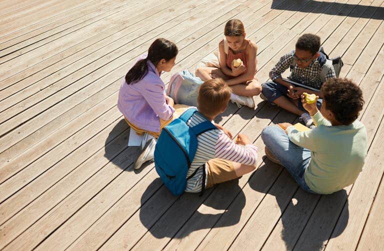 Five schoolchildren sitting outdoors, engaged in conversation.